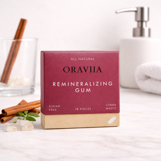 Box of Oraviiia remineralizing gum on a white surface with cinnamon sticks and a glass in the background.